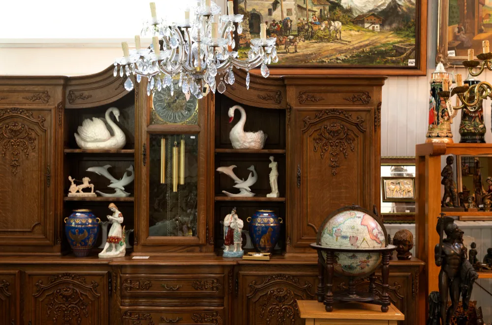 A wall of antique cabinets with porcelain swans, figurines, and a vintage globe — the kind of estate we appraise before clearing.